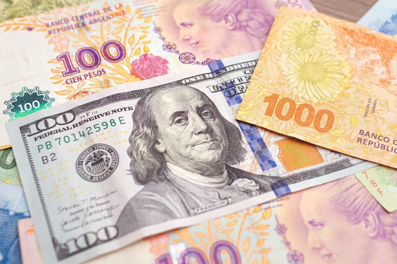 Argentine pesos and US dollar. Money, cash, exchange. Group of Argentine pesos banknotes with a 100 US dollar bill in close-up. Photograph representing the exchange between ARS and US DOLLAR. GETTY IMAGES/ISTOCKPHOTO
